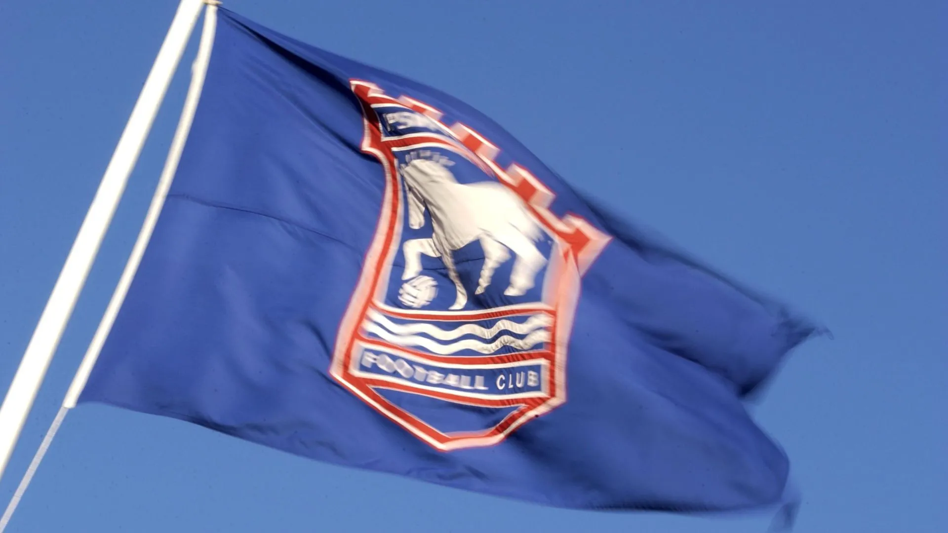 Biểu tượng hiện tại của Ipswich Town qua hình ảnh lá cờ tại sân Portman Road, tương phản với khái niệm huy hiệu mới từ AI